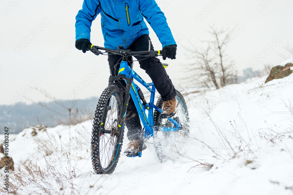Cyclist in Blue Riding Mountain Bike on Rocky Winter Hill Covered with Snow. Extreme Sport and Enduro Biking Concept. Cyclist in Blue Riding Mountain Bike on Rocky Winter Hill Covered with Snow. Extreme Sport and Enduro Biking Concept.