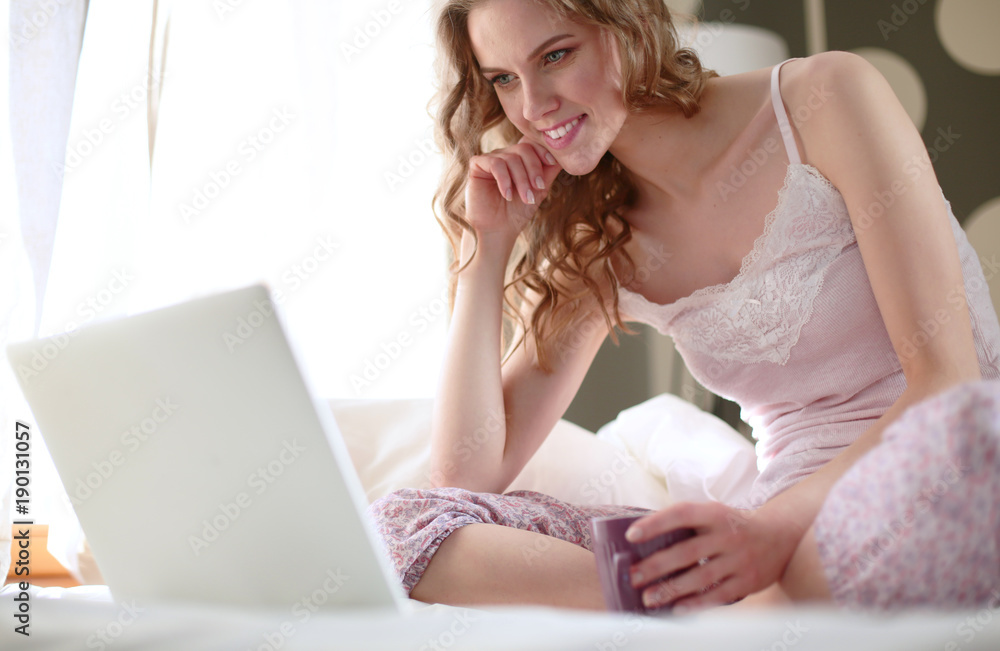 Naklejka premium Young beautiful woman sitting in bed with laptop.