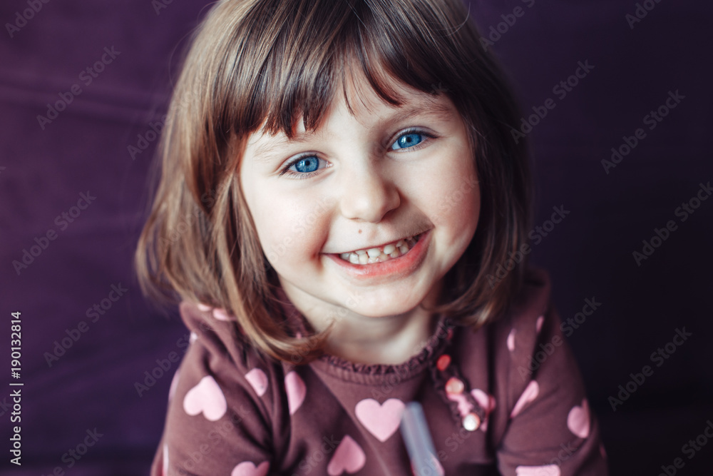 Closeup portrait of cute adorable white Caucasian smiling laughing girl with large blue eyes looking in camera