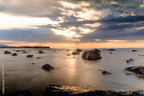 sun rays over the black sea and the cloud sky. Rocks in the water. Long exposition © nickzudwa