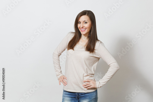 Beautiful European young happy brown-haired woman with healthy clean skin, dressed in casual light clothes, jeans looking at camera with shy charming smile on a white background. Emotions concept.