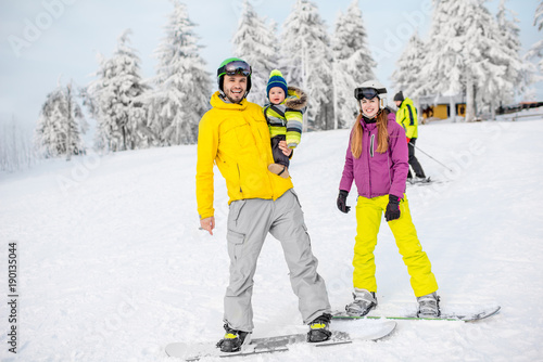 Portrait of a happy family with baby boy riding on the snowboards during the winter vacations on the snowy mountains
