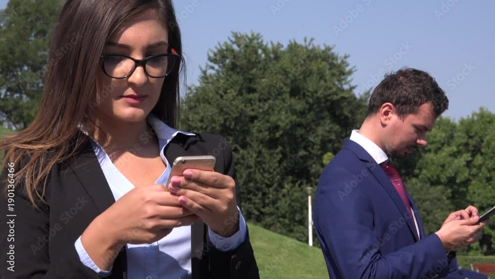 Business couple in the park using modern cell phone man woman fashionable suit Business couple in the park using modern cell phone man woman fashionable suit