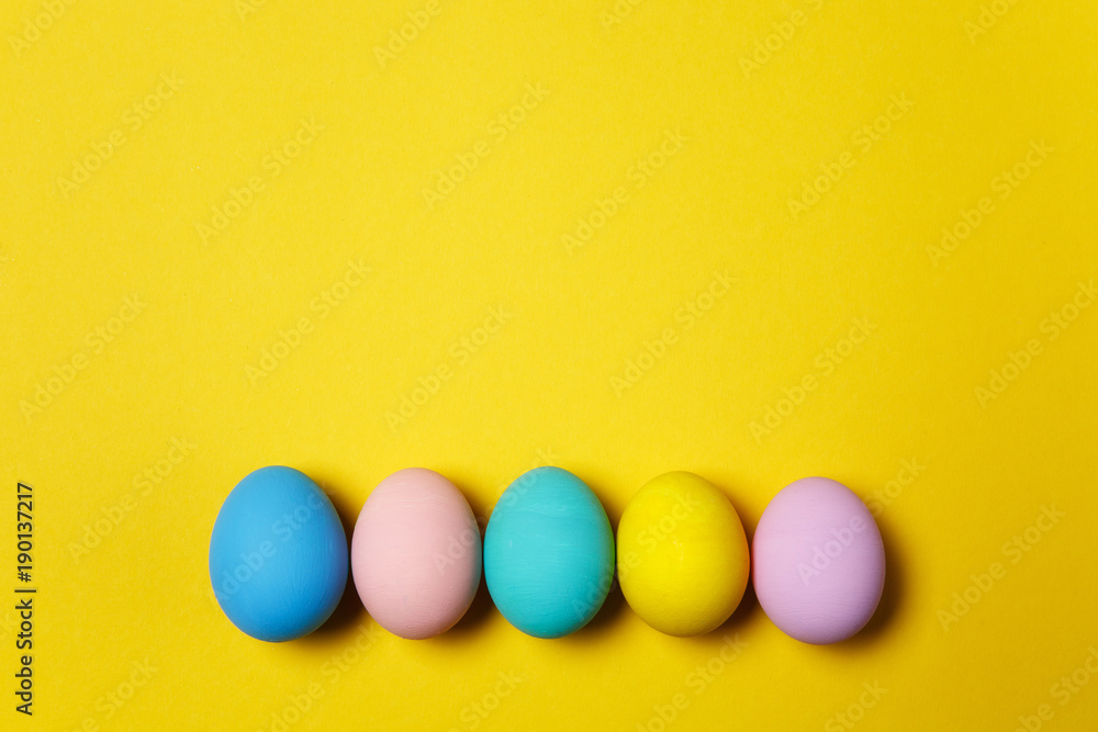 Row of five colorful pastel monophonic painted Easter eggs isolated on yellow background for card or postcard. Happy Easter concept. Copy space for advertisement. With place for text. Top view on eggs