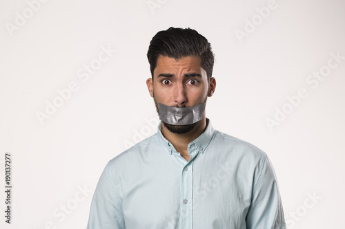 Portrait of a young man with tape on mouth over white background