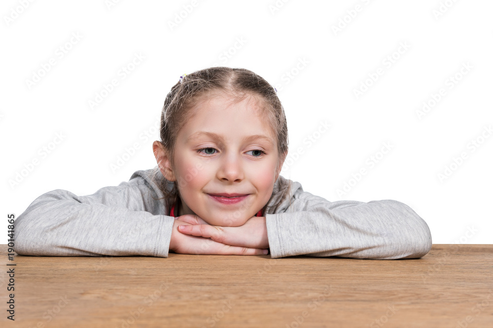 Portrait of a small beautiful girl leaning on the arm sitting at a table, isolated on a white background Portrait of a small beautiful girl leaning on the arm sitting at a table, isolated on a white background