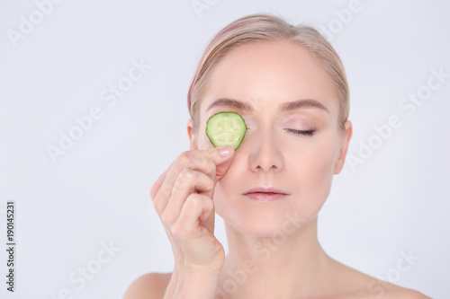 Young beautiful woman with cucumber slices on white background