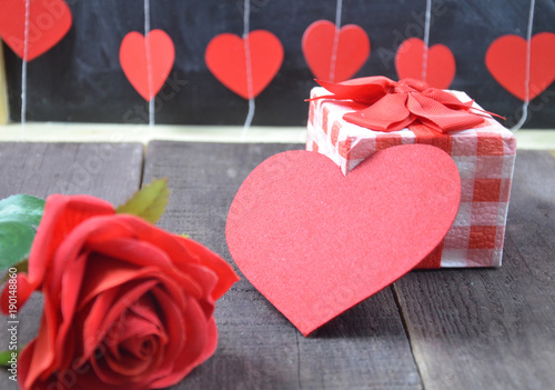 Gift or present box with red bow ribbon and glitter heart on wooden table for Valentines day