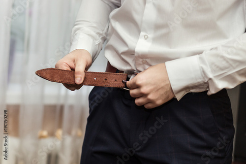 Businessman putting on a belt, fashion and clothing concept,groom getting ready in the morning before ceremony © bondvit