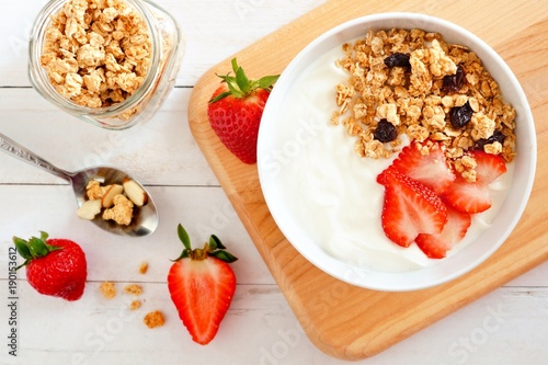 Yogurt with strawberries and granola. Table scene over a white wood background.