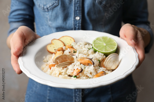Young woman holding plate with delicious seafood risotto on blurred background
