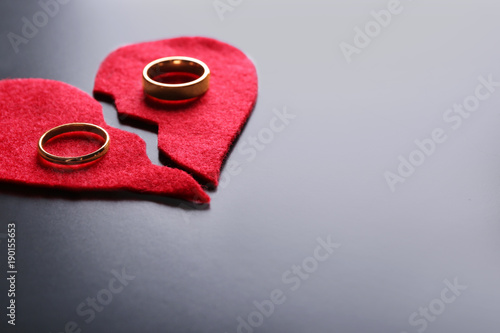 Fabric heart cut in half with wedding rings on grey background. Relationship problems