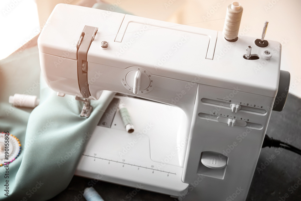 Naklejka premium Modern sewing machine with fabric and threads on table