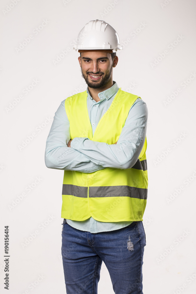 Happy confident bearded construction young man in helmet and vest standing with arms crossed, security and safety concept Happy confident bearded construction young man in helmet and vest standing with arms crossed, security and safety concept