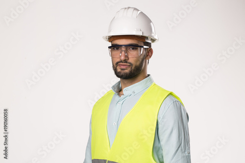 arabic latin engineer worker serious looking to camera , wearing security helmet glasses and vest , isolated on white