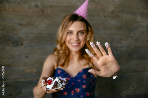 Beautiful funny girl in festive hat showing her palm in cream after eating a birthday cake.