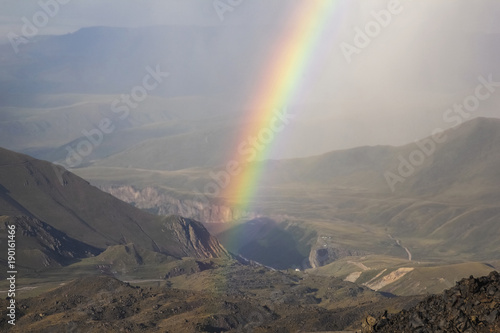 Rainbow over the mountains with rainy cloudy sky. Valleys, meadows glades and ridges.