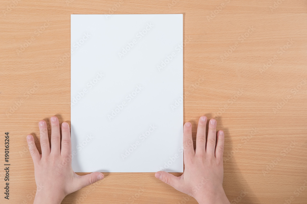 blank sheet of paper with place for your text lying on the table with the hands of a child blank sheet of paper with place for your text lying on the table with the hands of a child