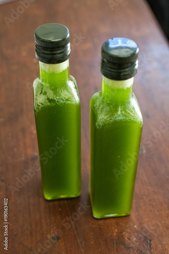 Top view of two bottles of fresh green oil on a brown wooden table