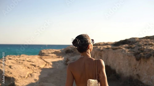 Beautiful brunette woman goes to the sea through the rocks in Cyprus photo