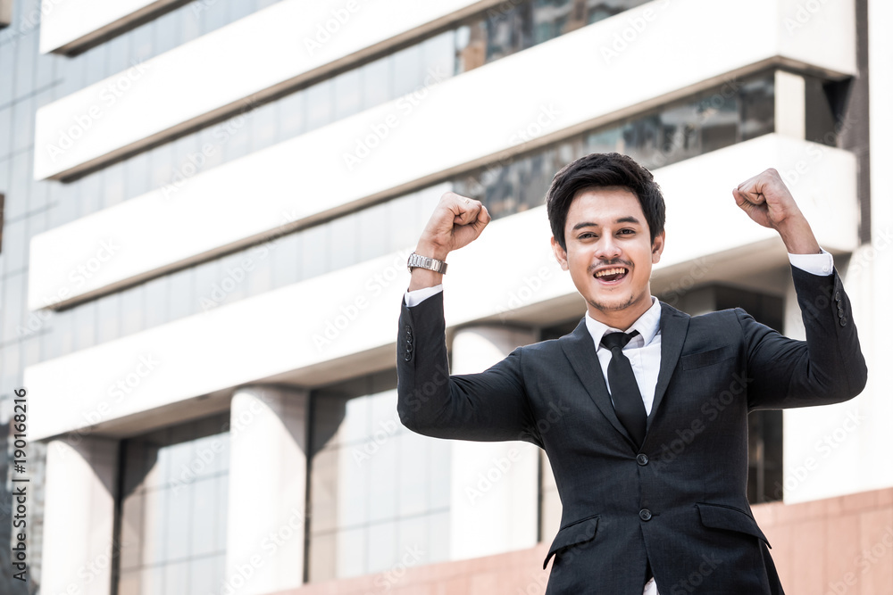Portrait of young Asian businessman in black suit standing with office building background. Free space for text Portrait of young Asian businessman in black suit standing with office building background. Free space for text