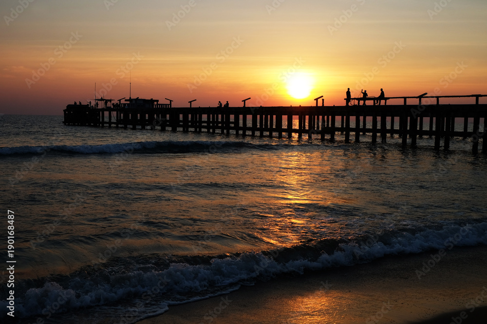 Beautiful silhouette of wooden bridge walkway and people doing their activities over the sea water wave and beach during sunset
