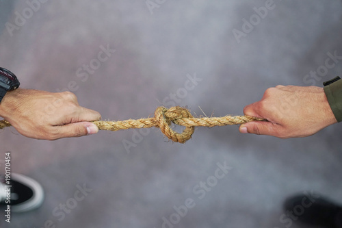 Tug War concept.Two Men pulling the rope with knot in opposite directions.
