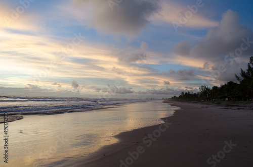 view of the blue sky and full of morning clouds on a beach with sea water reaching in the sand.