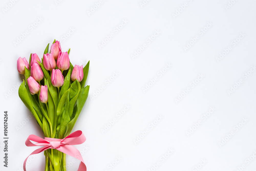 Top view of pink tulips bouquet, wrapped with pink ribbon over white background. Copy space.
