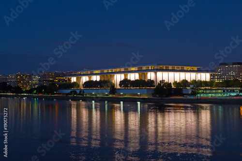 Washington DC night panorama with John F. Kennedy Center for the Performing Arts in the center of the frame. Brightly lit The Kennedy Center with reflection in dark waters of Potomac River.