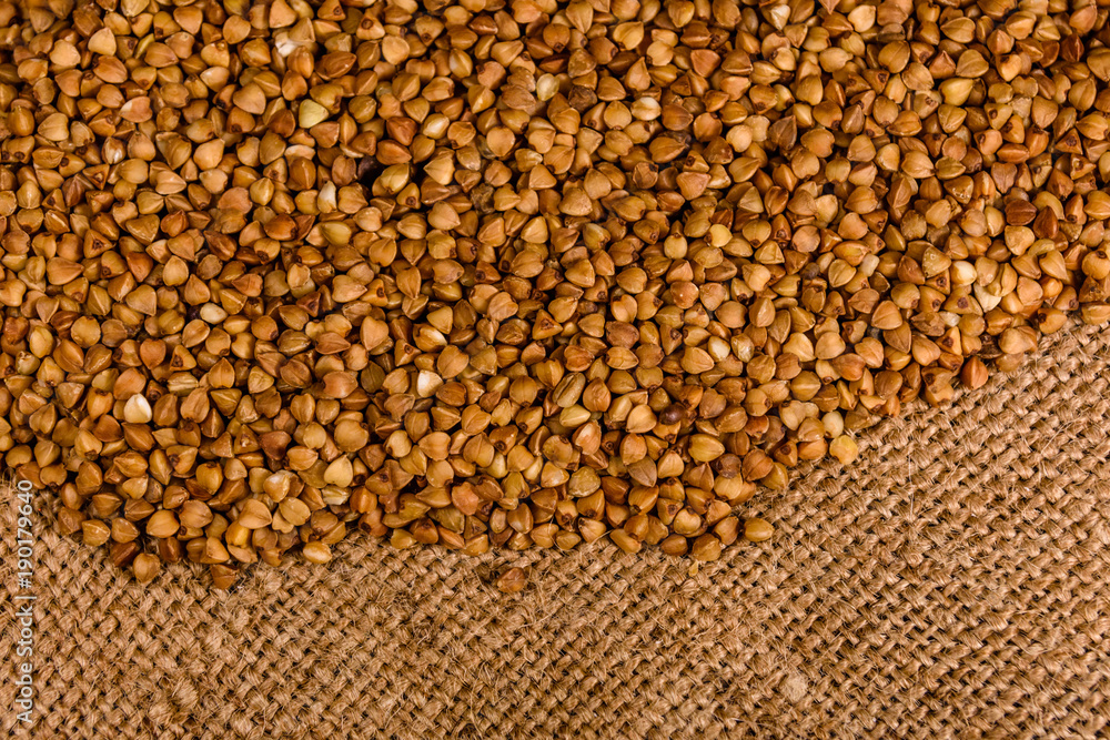 Fototapeta premium Pile of the raw buckwheat on sackcloth. Top view