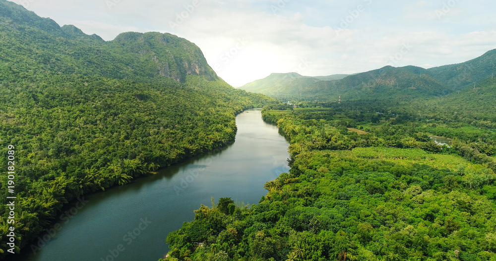 Aerial view of river in tropical green forest with mountains in background - obrazy, fototapety, plakaty 