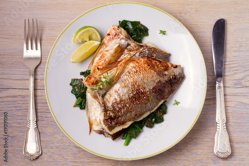 Roasted sea bream with spinach. Dorado or dorada fish fillet on white plate