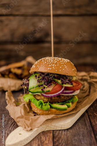 Tasty vegan burger with fresh vegetables on dark rustic wooden table, selective focus. Healthy fast food background with space for text.
