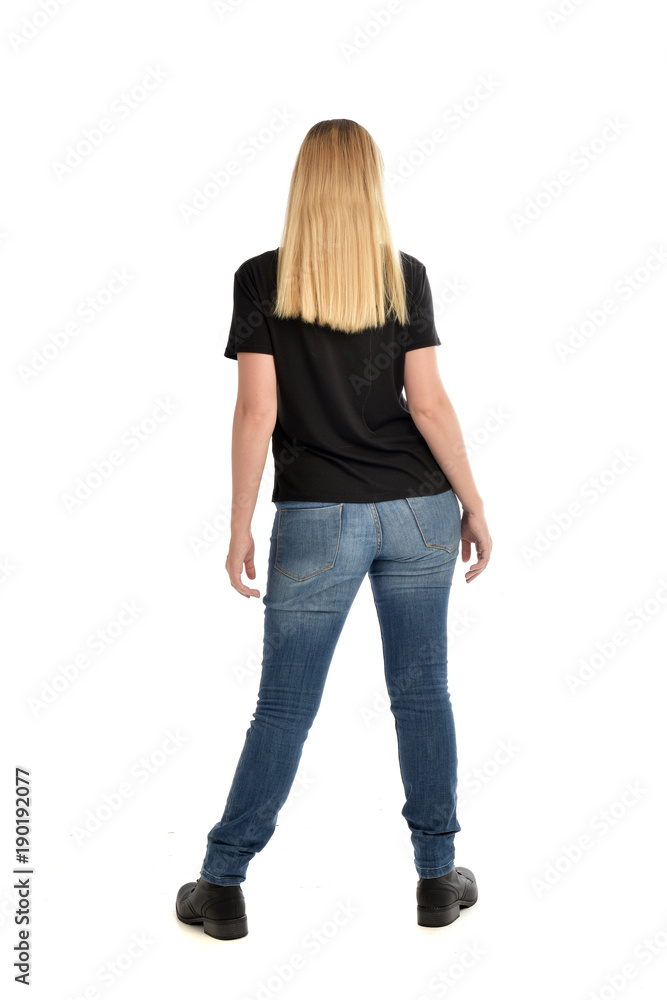 full length portrait of blonde girl wearing simple black shirt and jeans, standing pose wit back to the camera.. isolated on white studio background. full length portrait of blonde girl wearing simple black shirt and jeans, standing pose wit back to the camera.. isolated on white studio background.