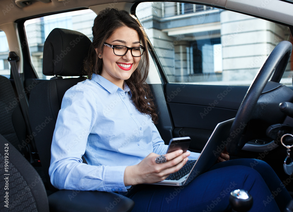 Beautiful young business woman using laptop and phone in the car.	