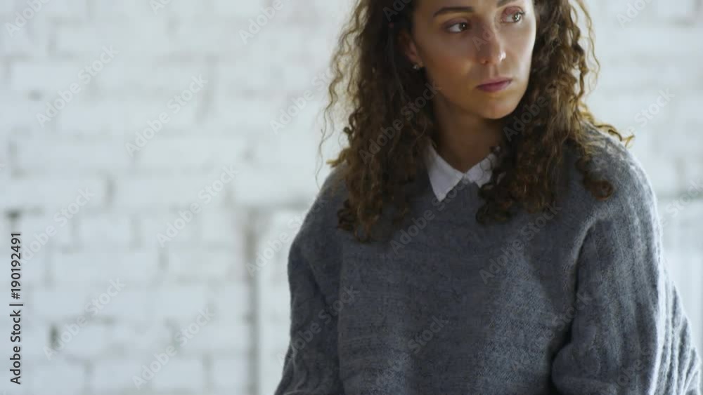 Tilt up of sad young woman with curly hair holding paper handkerchief and listening to someone talk during support group meeting Tilt up of sad young woman with curly hair holding paper handkerchief and listening to someone talk during support group meeting