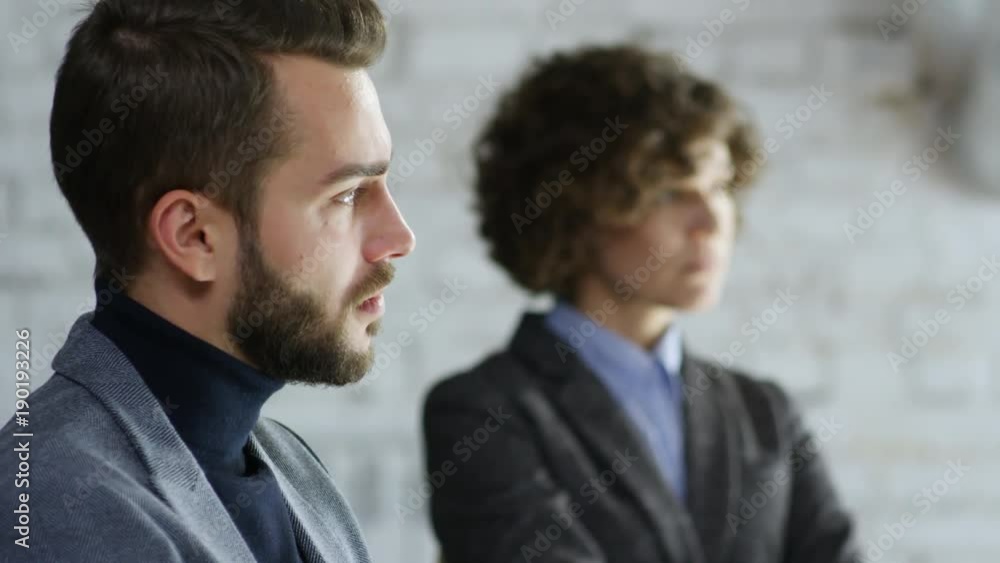 Tilt up with rack focus of bearded male psychotherapist with clipboard and young female patient with curly hair listening to someone talk during support group meeting Tilt up with rack focus of bearded male psychotherapist with clipboard and young female patient with curly hair listening to someone talk during support group meeting