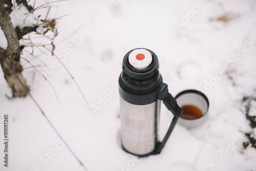 woman hands pours hot tea or coffee out of thermos on winter forest background.