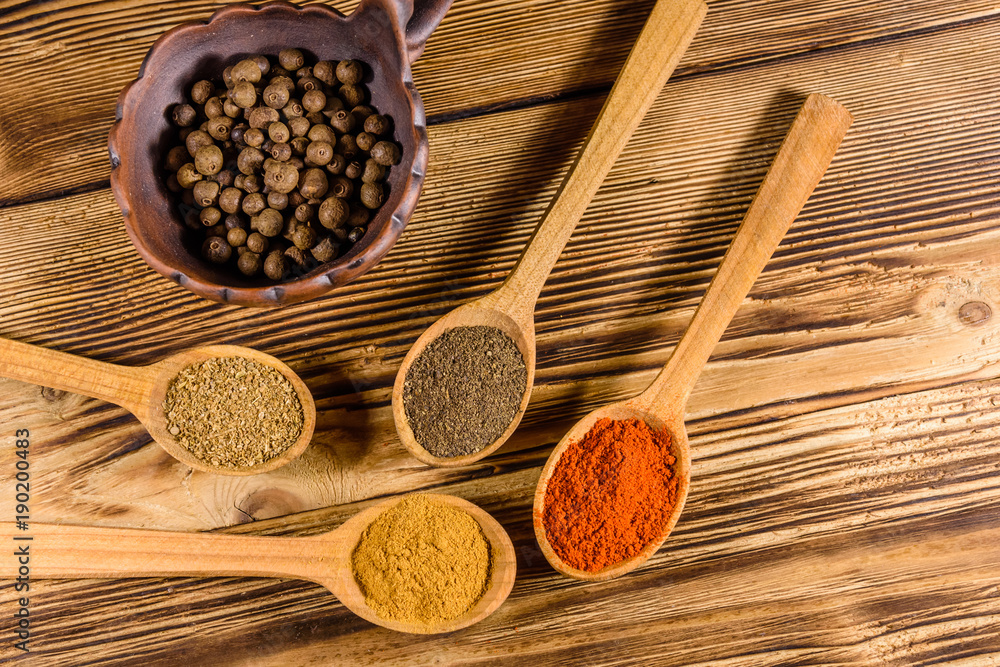 Ceramic bowl and spoons with the different spices on wooden table. Top view Ceramic bowl and spoons with the different spices on wooden table. Top view