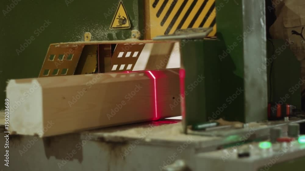 Woodworker puts wooden bar into precise cutting machine with laser pointer at sawmill production, close up Woodworker puts wooden bar into precise cutting machine with laser pointer at sawmill production, close up