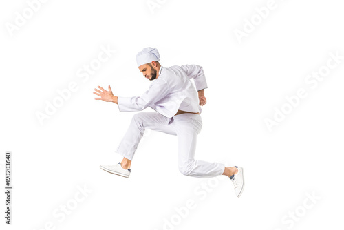side view of young chef running and jumping isolated on white