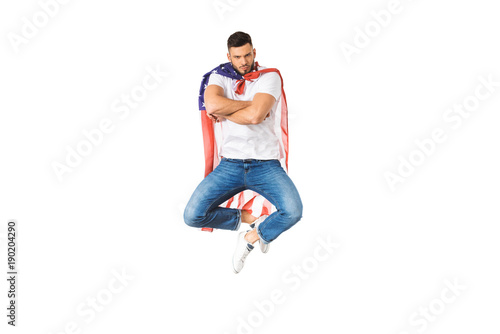 handsome young man with american flag jumping with crossed arms and looking at camera isolated on white