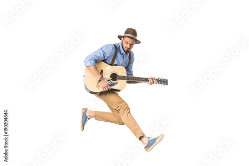 handsome young man in hat playing guitar and jumping isolated on white