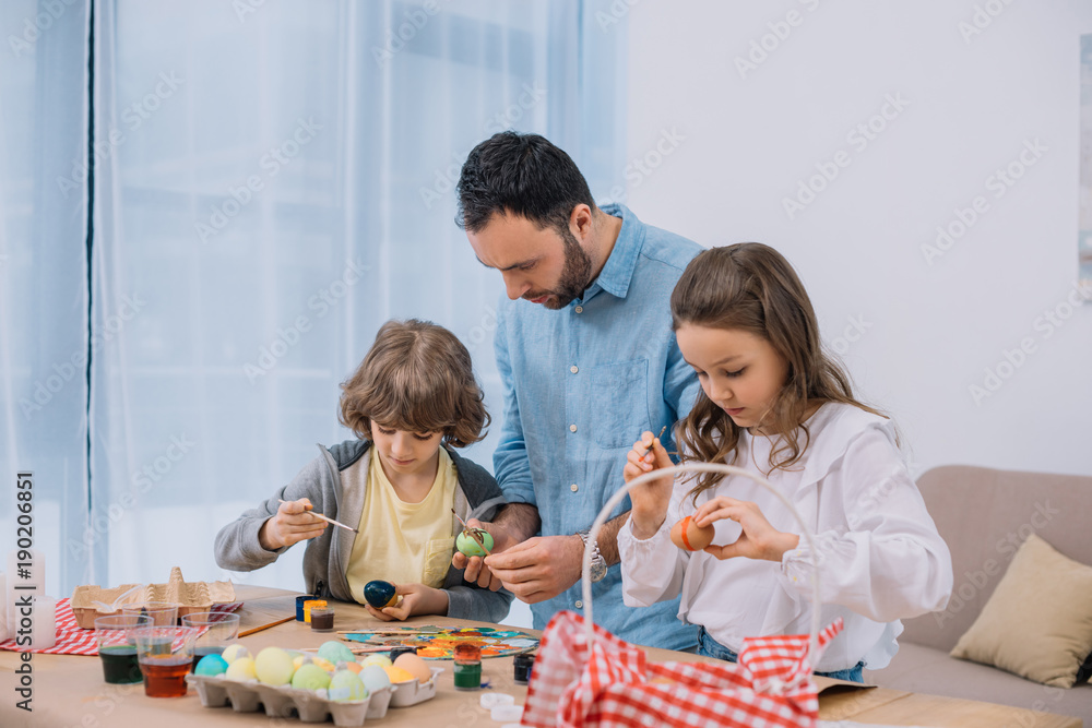 Fototapeta premium young father and children painting eggs for easter holiday
