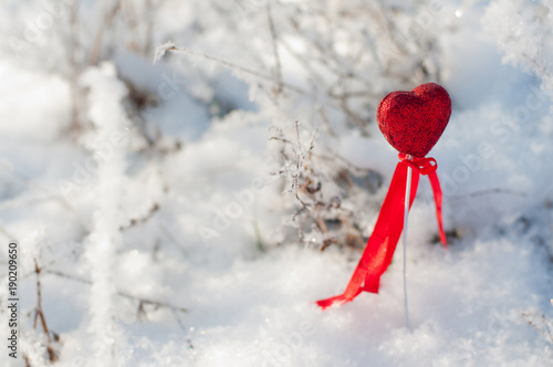 St. Valentine's day concept. Red heart with ribbon in white winter snow