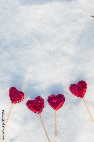 Love greeting concept. Top view on four red hearts on wooden sticks laying on white textured snow in sunny winter day