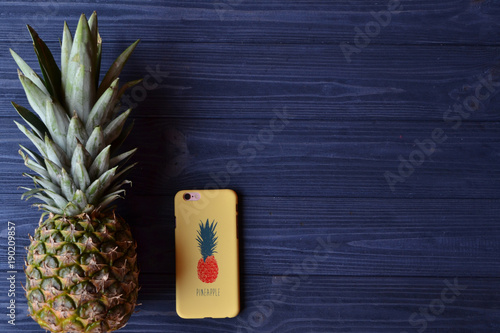 Pineapple and smartphone on the dark blue wooden table. Summer flat lay. Background with place for text.