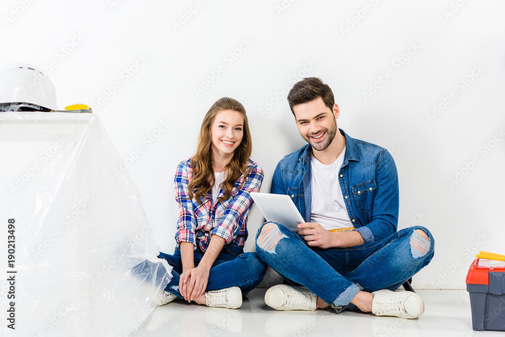 smiling couple sitting with tablet and looking at camera smiling couple sitting with tablet and looking at camera