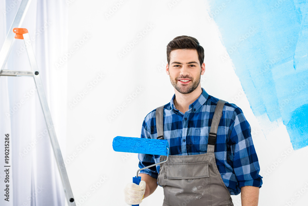 smiling man standing with paint roller brush and looking at camera smiling man standing with paint roller brush and looking at camera